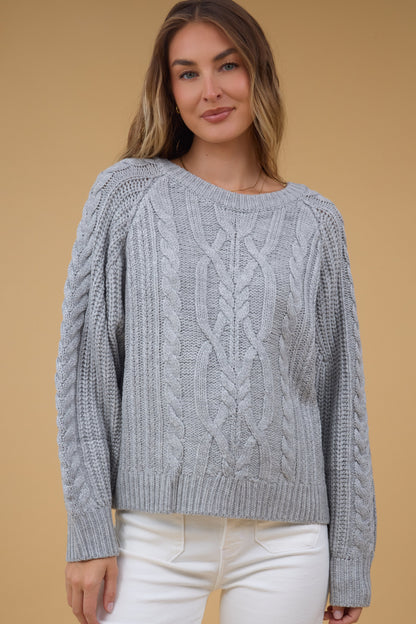 Woman wearing a grey sweater with multiple types of cables with cable knit sleeves also.