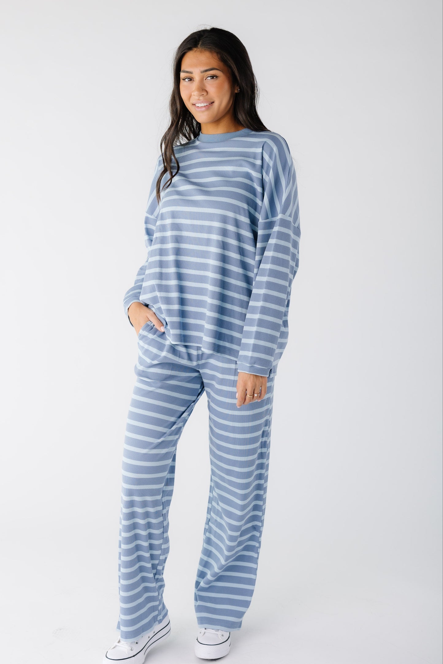 Young woman wearing a light blue stripe, loose fitting lounge set with long sleeves and long, wide leg pants.
