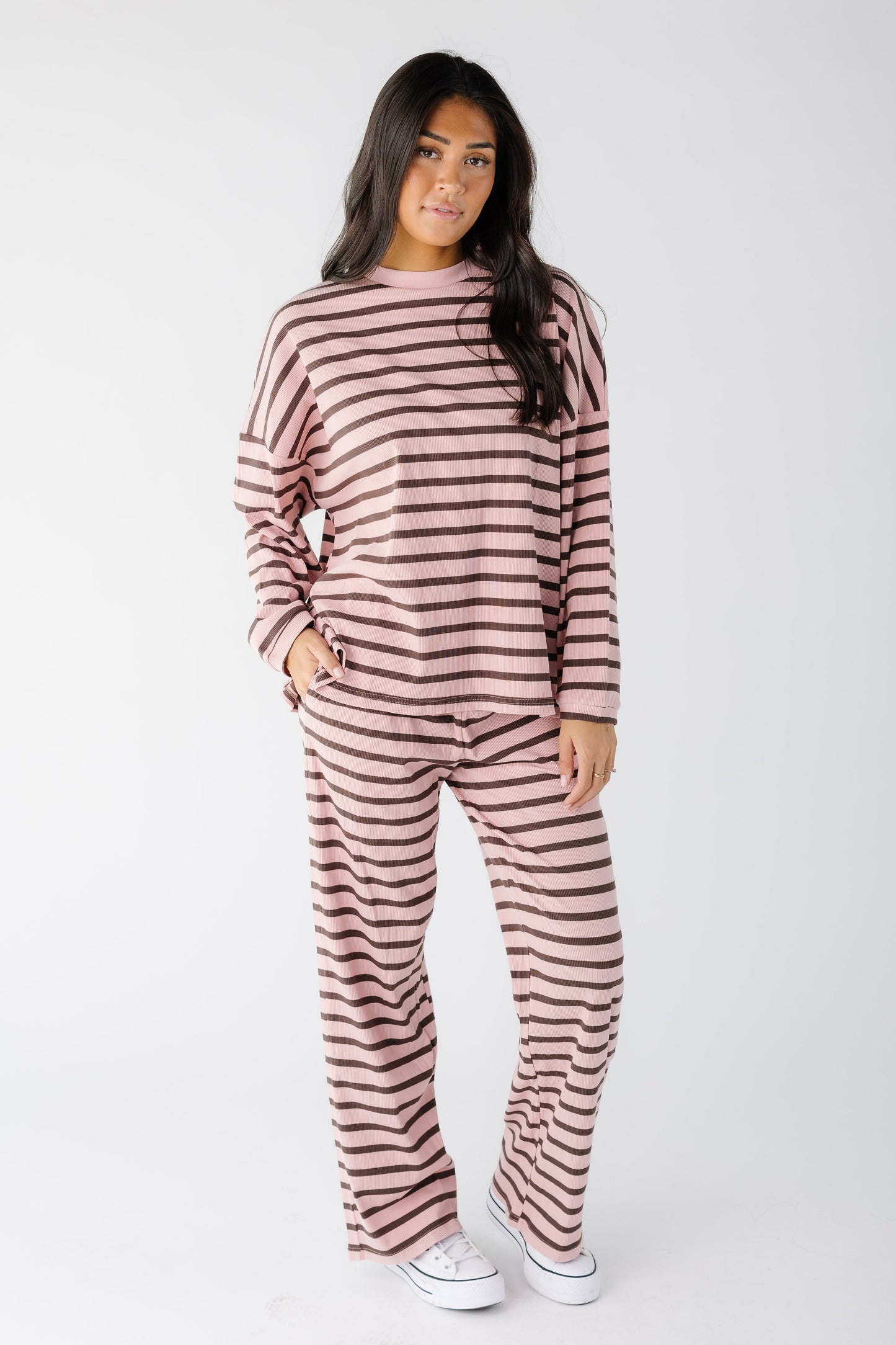 Woman wearing a modest loose fitting ribbed lounge set in pink and brown with long sleeves and a crew neckline.