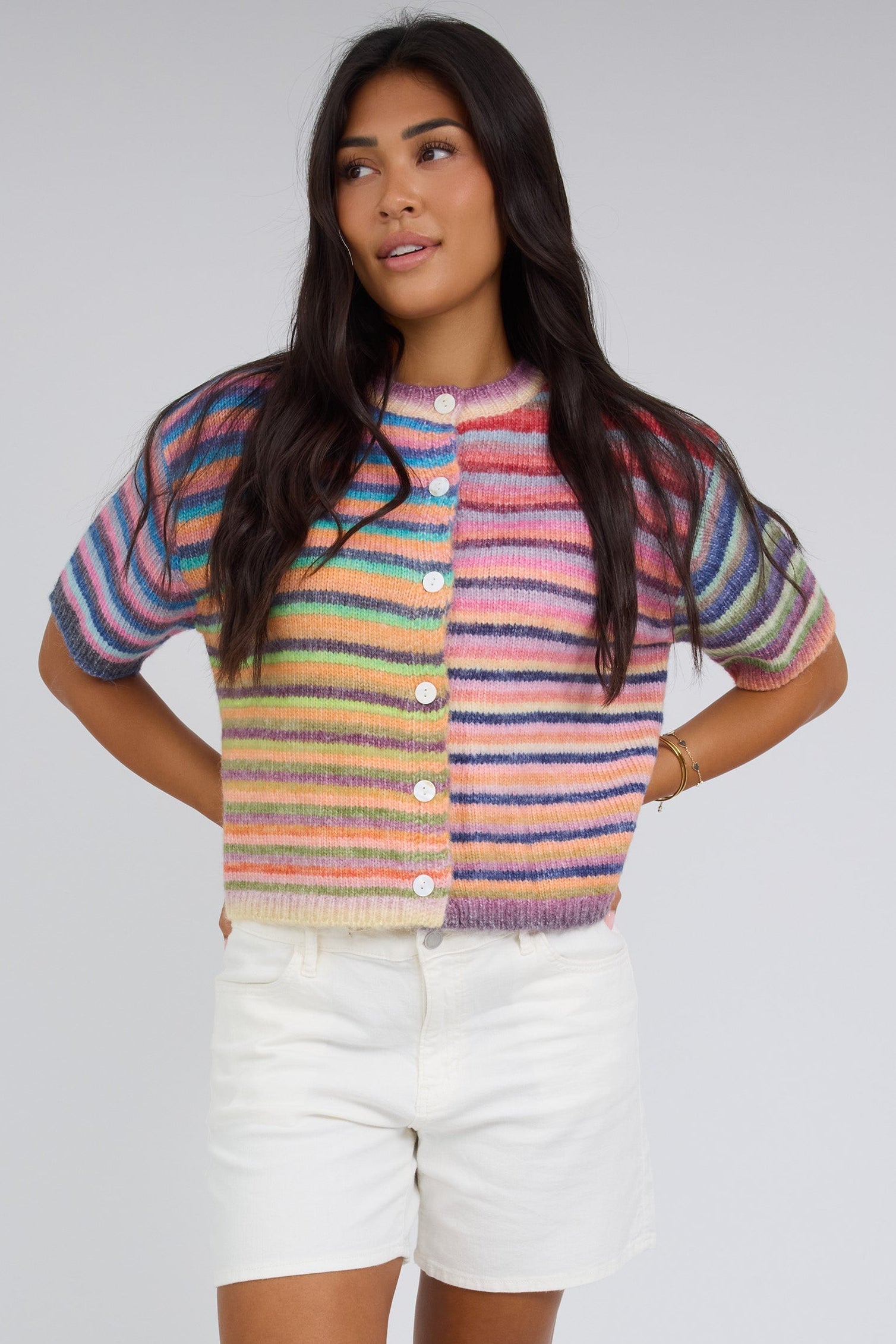 Woman wearing a bright rainbow button down cardigan with a crew neckline and short sleeves.