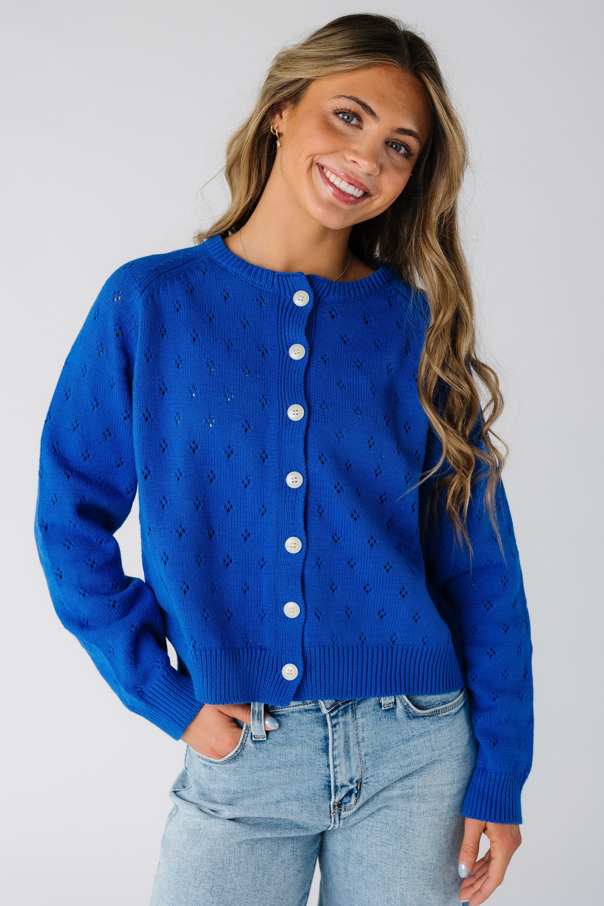 Young woman wearing an eyelet knit button down cardigan with long sleeves in royal blue.
