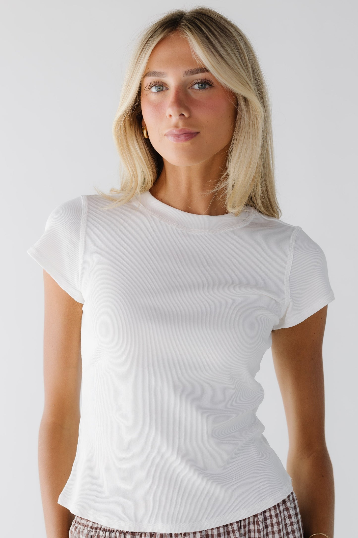 Young woman wearing a white close fitting top with short sleeves and a wide ribbed neckline.