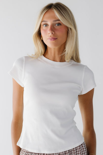 Young woman wearing a white close fitting top with short sleeves and a wide ribbed neckline.