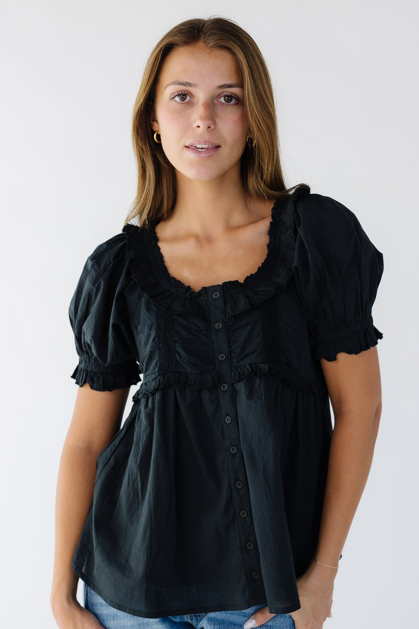 Woman wearing a loose fitting blouse with a scoop ruffled neckline  and short puff sleeves.