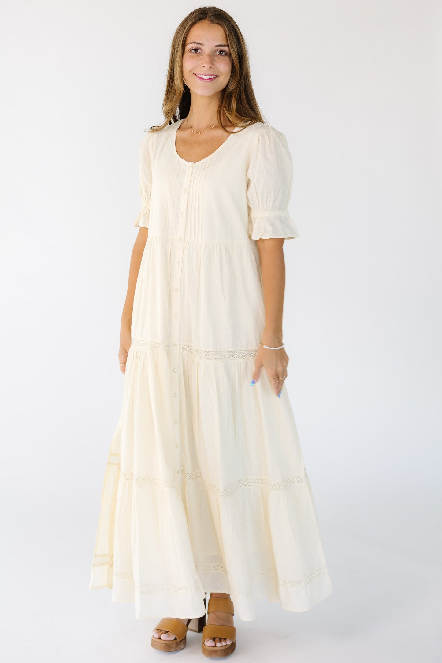 Woman wearing a modest cream loose fitting button down dress with short sleeves and multiple gathered tieres.