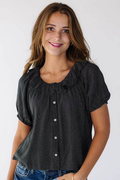 Young woman wearing a modest black and white polkadot button down top with a ruffled collar.
