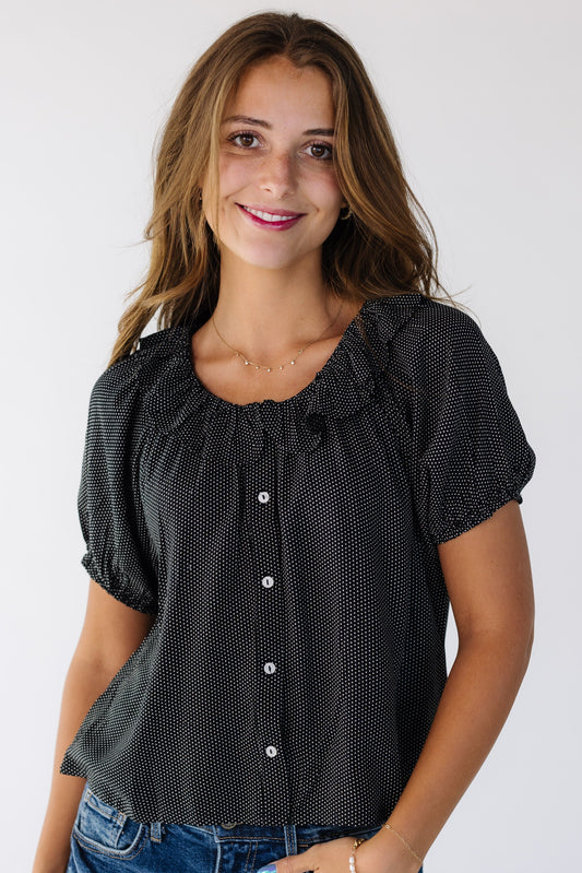 Young woman wearing a modest black and white polkadot button down top with a ruffled collar.