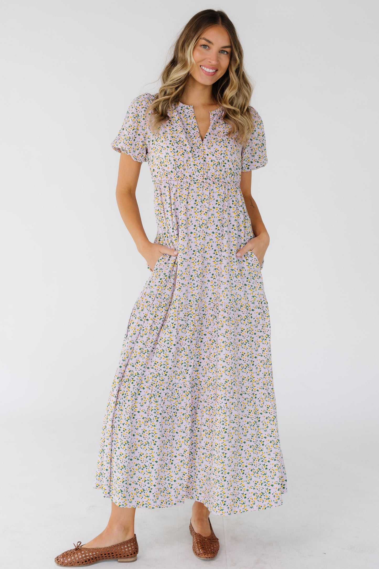 Young woman wearing a modest light lavender midi dress in a multicolor floral print, short puff sleeves, V-neckline and an empire waist.