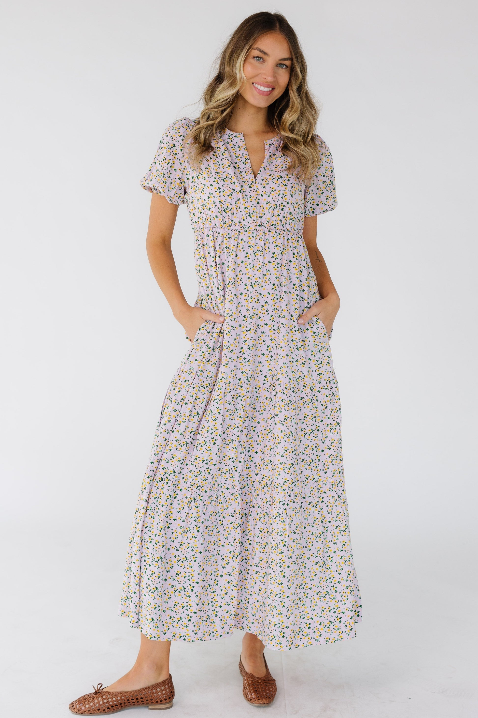 Young woman wearing a modest light lavender midi dress in a multicolor floral print, short puff sleeves, V-neckline and an empire waist.