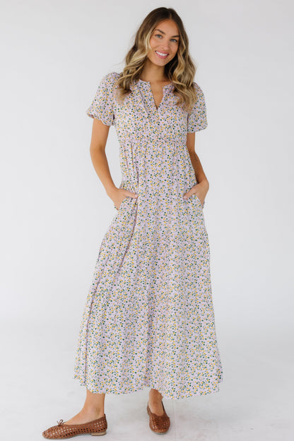 Young woman wearing a modest light lavender midi dress in a multicolor floral print, short puff sleeves, V-neckline and an empire waist.