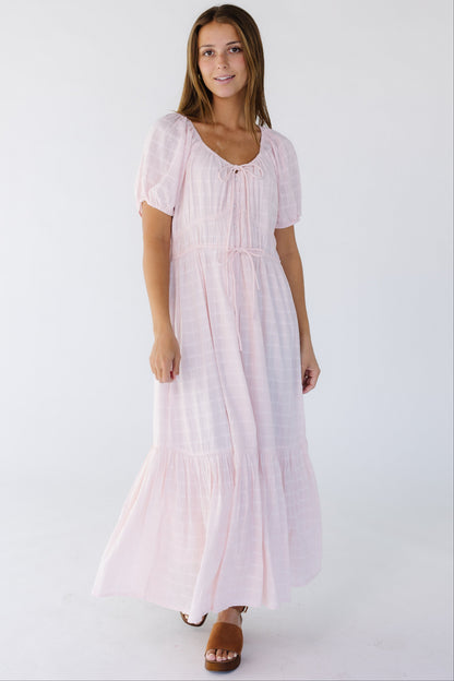 Young woman wearing a light pink midi-maxi dress with a textured plaid pattern with a scoop neckline, short puff sleeves and a full skirt.