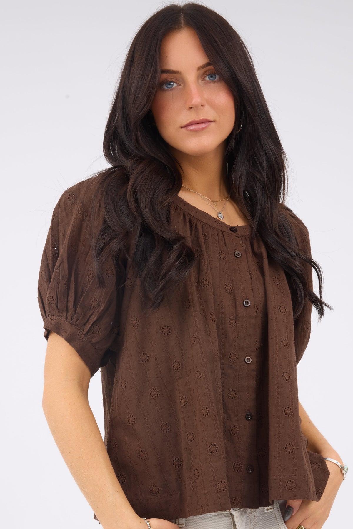 A young woman wearing a modest brown eyelet, button down blouse with short sleees.