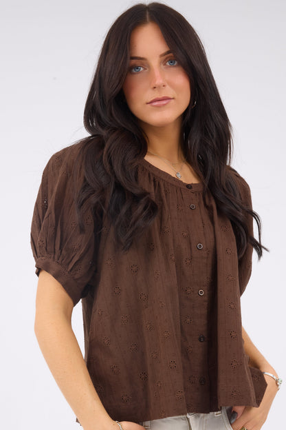 A young woman wearing a modest brown eyelet, button down blouse with short sleees.