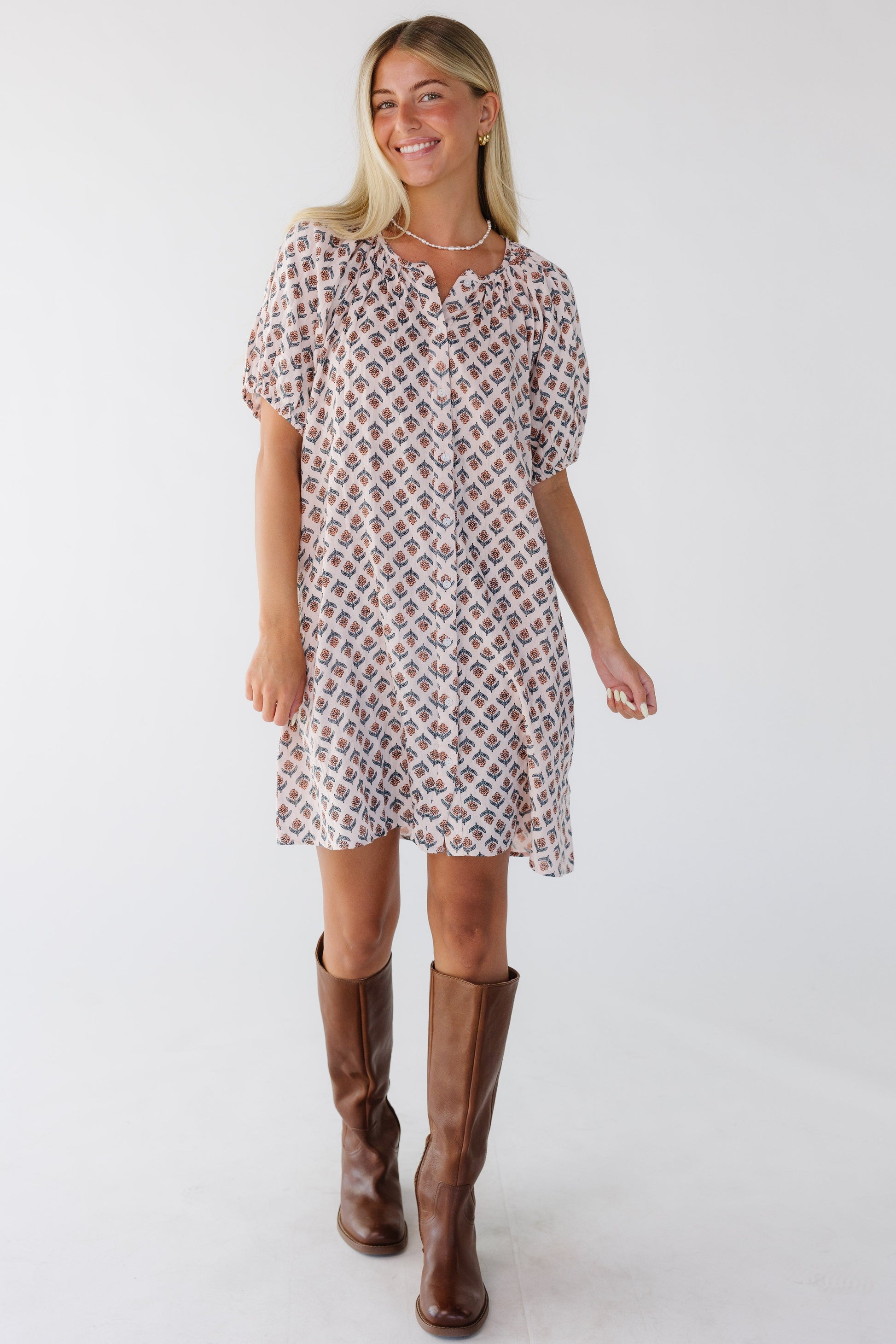 Woman wearing a short modest loose fitting button down dress with short sleeves and a round neckline in pink floral print.