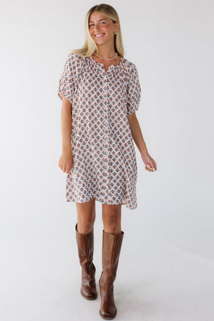 Woman wearing a short modest loose fitting button down dress with short sleeves and a round neckline in pink floral print.