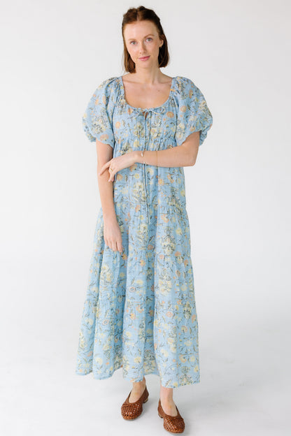 Woman wearing a blue floral tiered midi dress with a scoop neckline and short balloon sleeves.