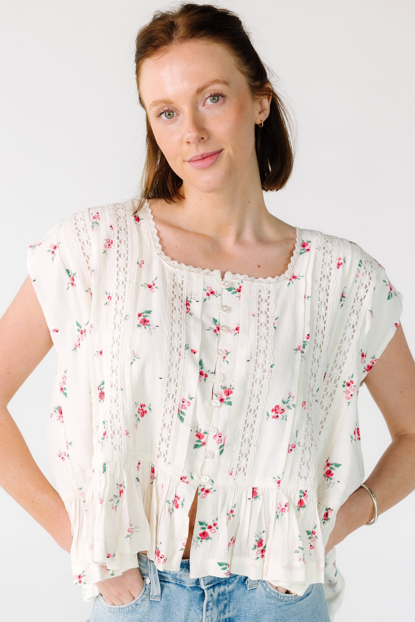 Young woman wearing a modest ivory blouse with red floral print, a lace trimmed button down blouse with lace insets and a bottom ruffle.
