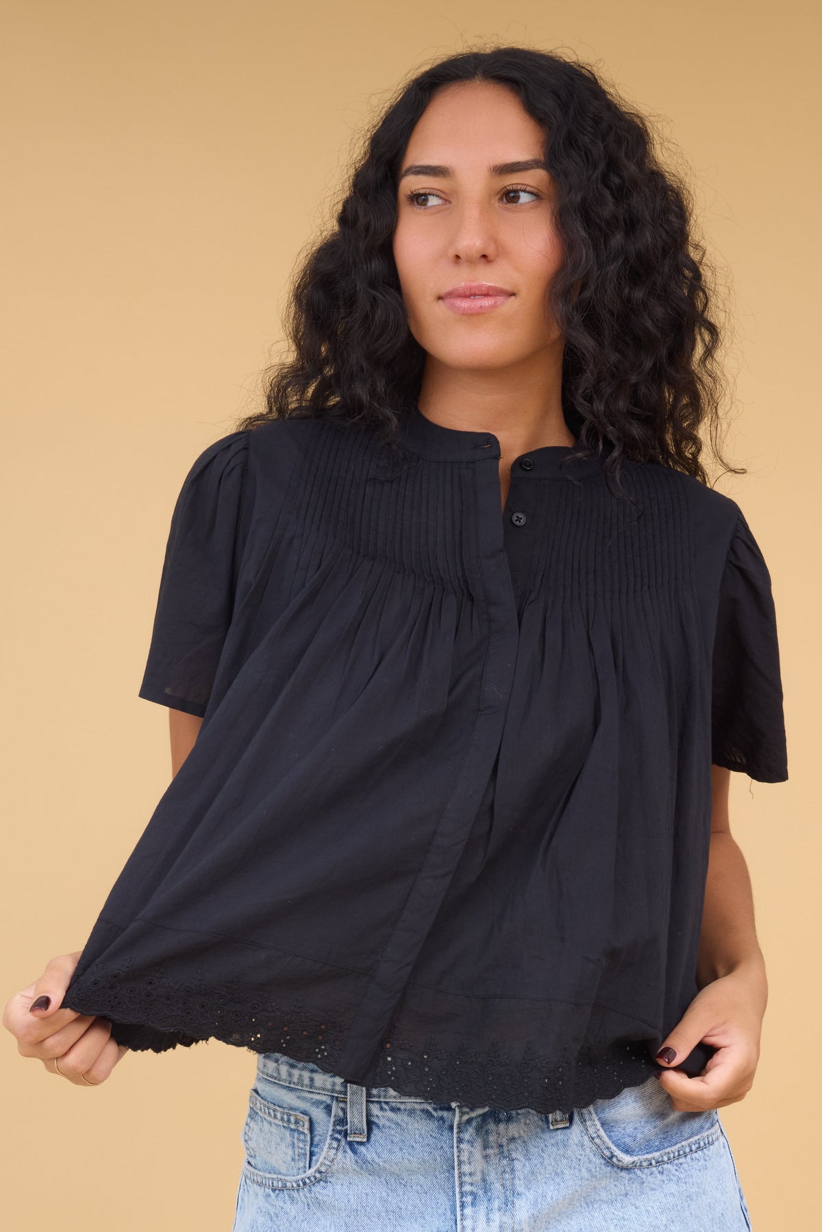 Young woman wearing a modest black button down blouse with pintucks at the yoke, short sleeves and bottom lace trim.