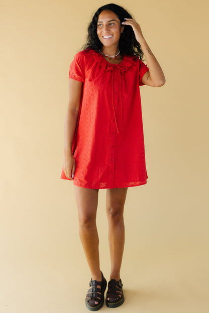 Young woman wearing a short red eyelet dress with a round ruffled collar and short sleeves.