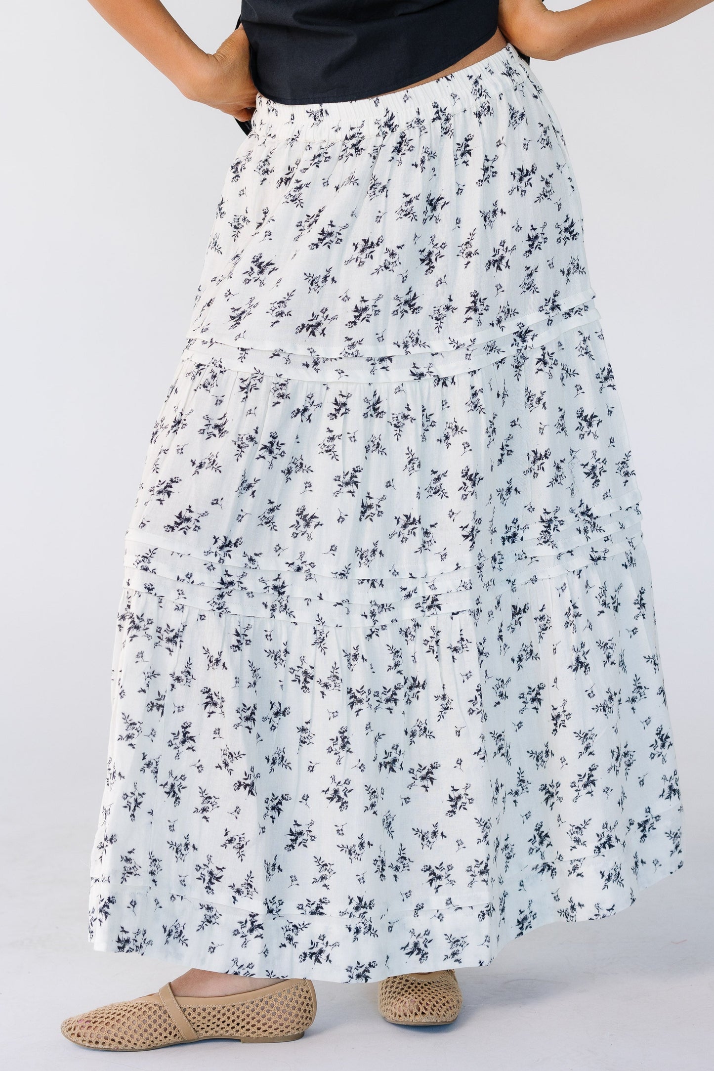 Woman wearing a white tiered midi skirt with black floral print, pleats and tiers.