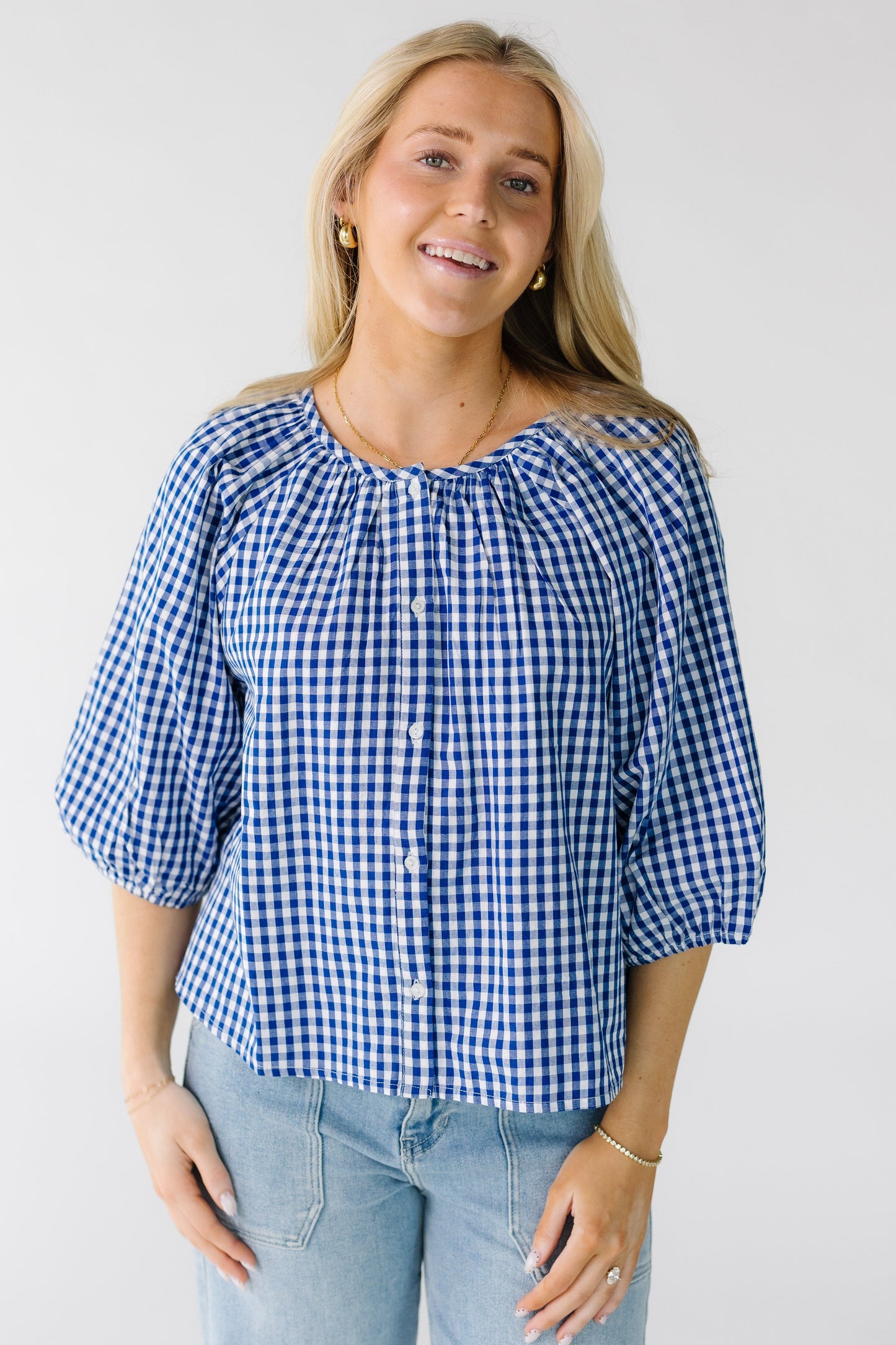 Woman wearing a loose fitting button down blouse in royal and white gingham with half length sleeves.