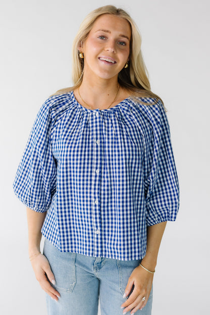 Woman wearing a loose fitting button down blouse in royal and white gingham with half length sleeves.