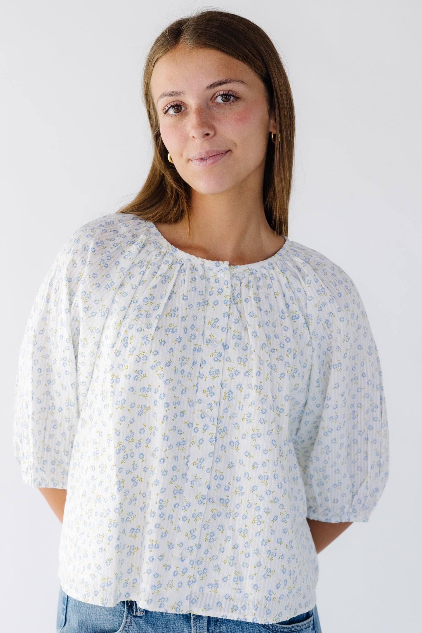 Woman wearing a white and blue floral print button down swing top with elbow length sleeves.