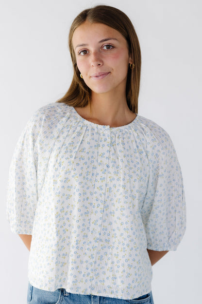 Woman wearing a white and blue floral print button down swing top with elbow length sleeves.