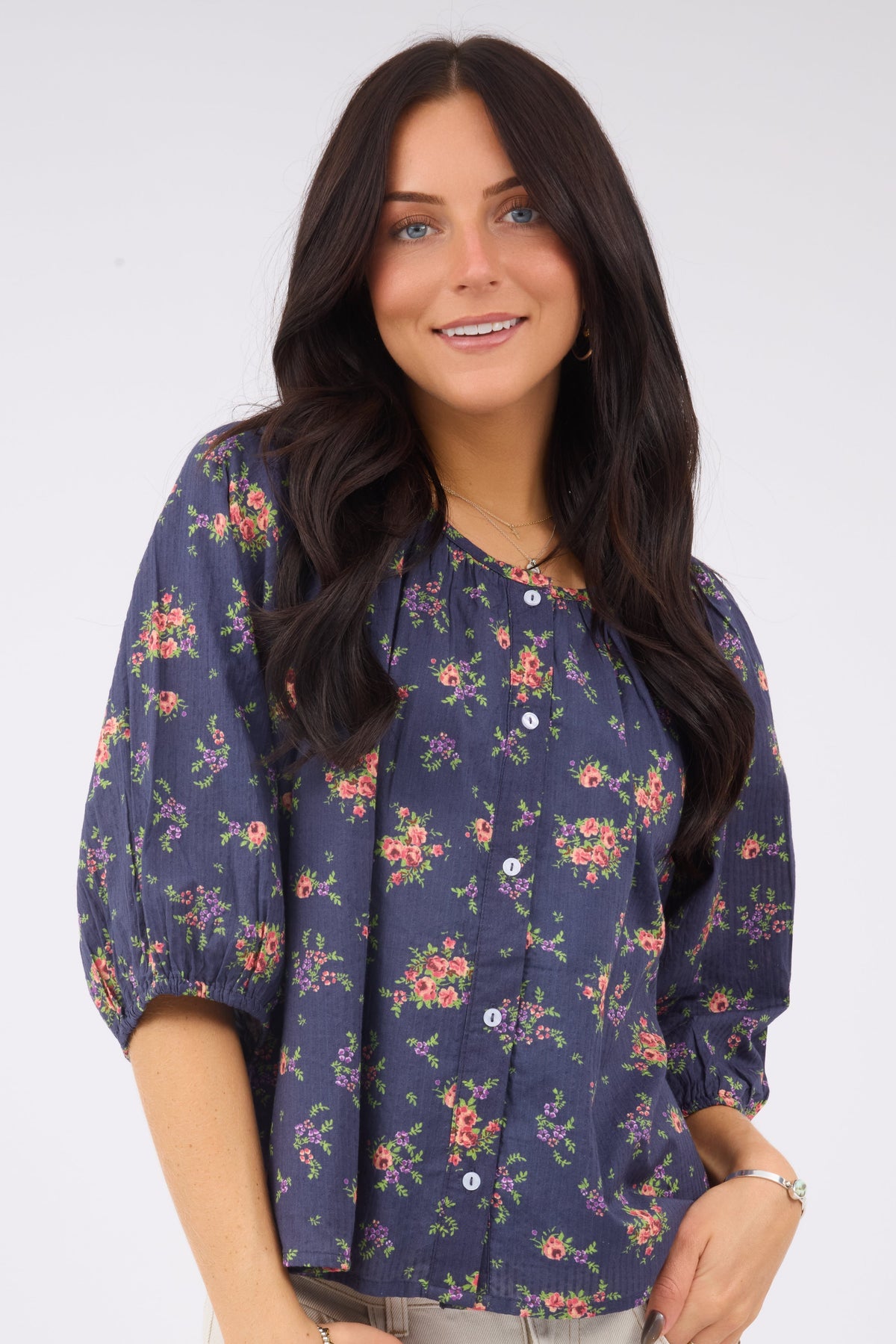 A young woman wearing a loose fitting button down blouse with elbow length sleeves and a wide round neckline.
