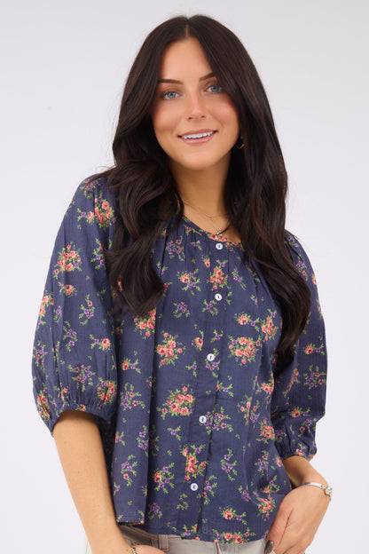 A young woman wearing a loose fitting button down blouse with elbow length sleeves and a wide round neckline.