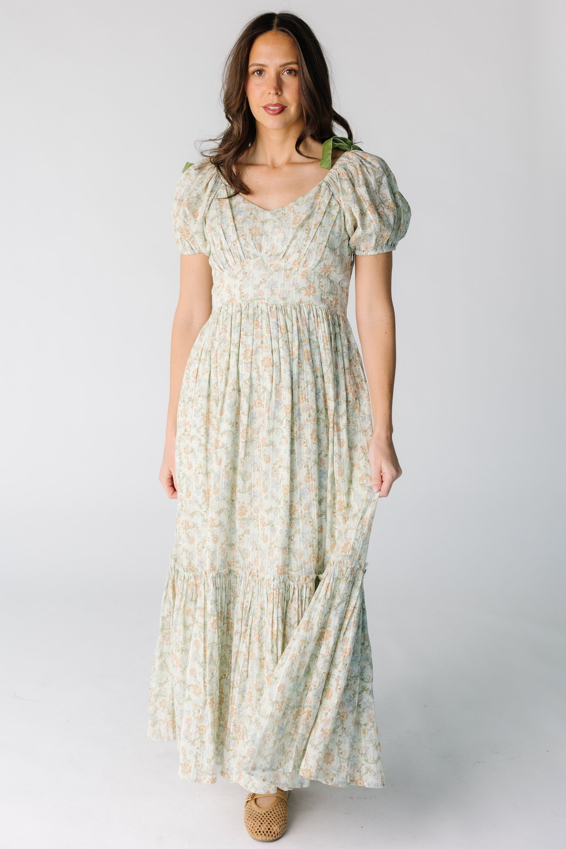 Woman wearing a modest green floral print midi-maxi dress with short puff sleeves and a wide bottom ruffle.