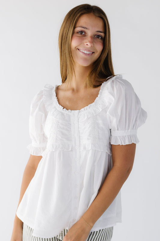Young woman wearing a modest white ruffle and lace button down blouse with a ruffled scoop neckline, short puff sleeves.