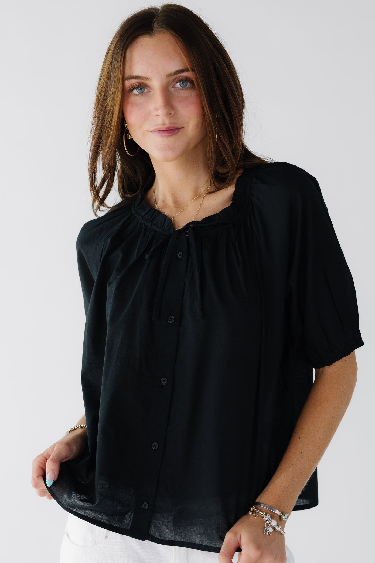 Young woman wearing a modest loose fitting button down top in black with short full sleeves and a stand up ruffle collar and tie.