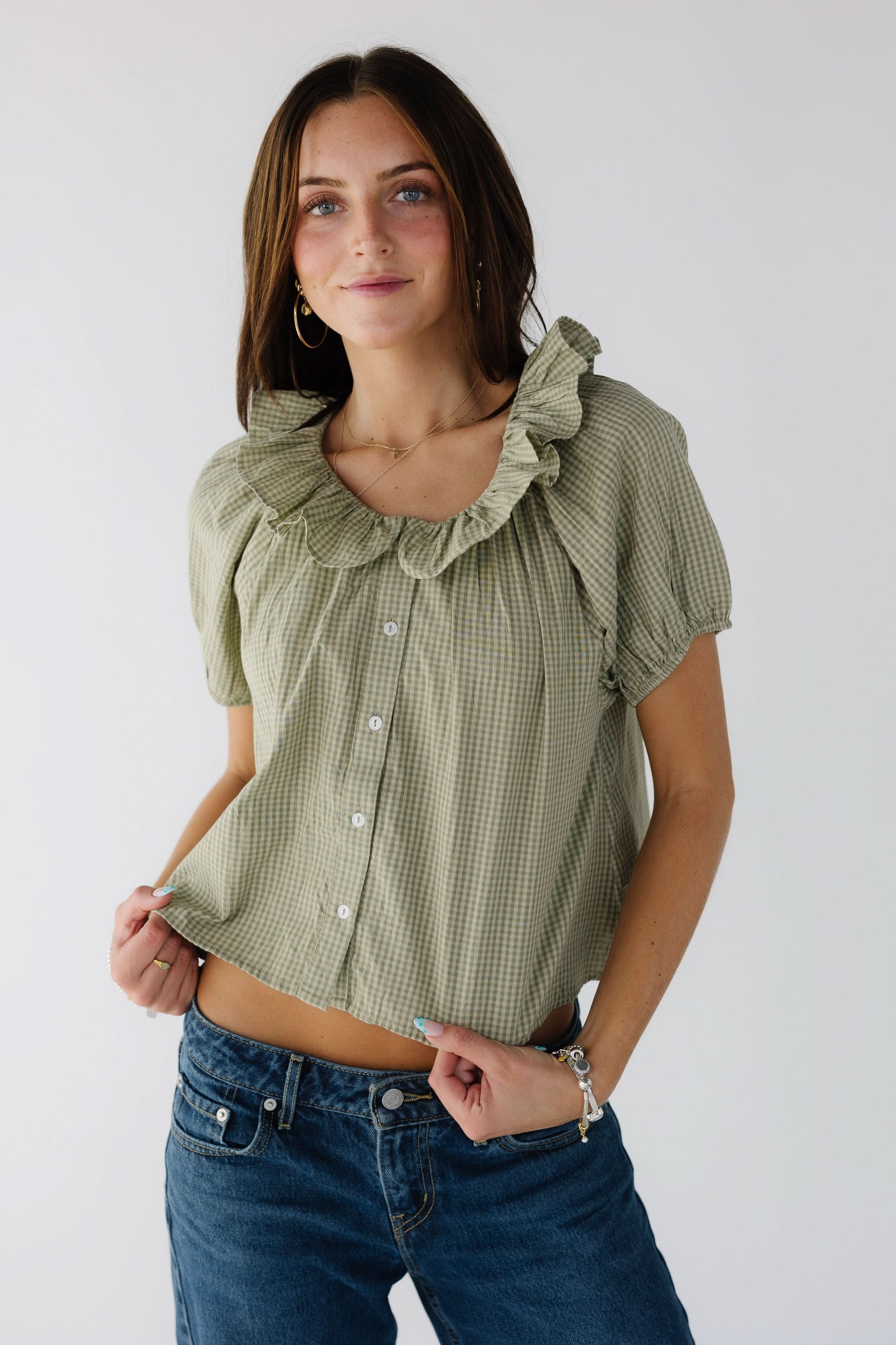 Young woman wearing an olive button down top with short sleeves and a ruffle collar.
