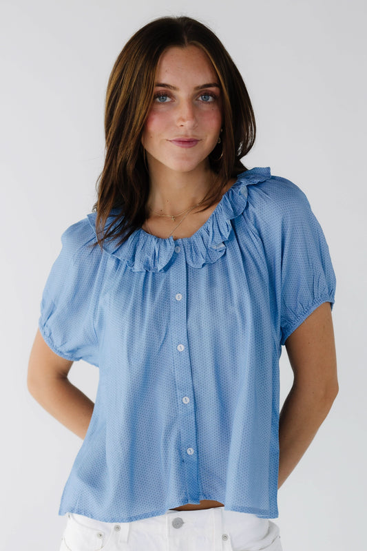 Young woman wearing a blue polka dot button down blouse with short puff sleeves and a round ruffled collar.