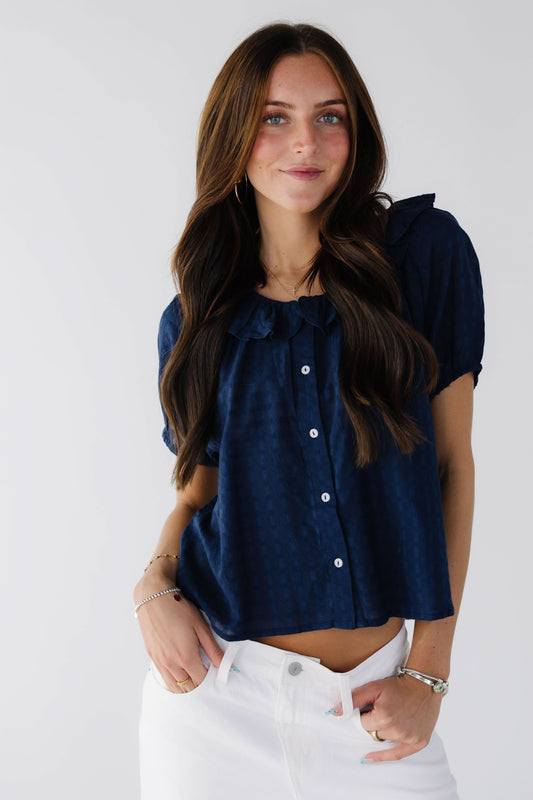 Young woman wearing a modest navy button down blouse with a ruffle collar and short sleeves.