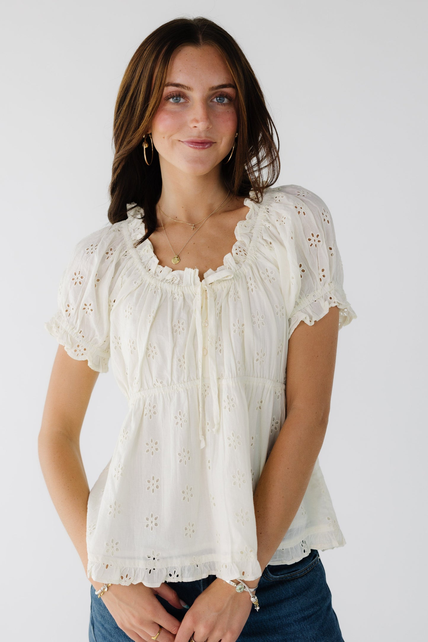 Young woman wearing a cream all eyelet top with short sleeves, and a ruffled scoop neckline.