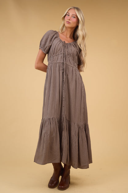 Young woman wearing a brown & white gingham midi dress with a drawstring scoop neckline, short puff sleeves and gathered-drawstring waist details with a wide bottom ruffle.