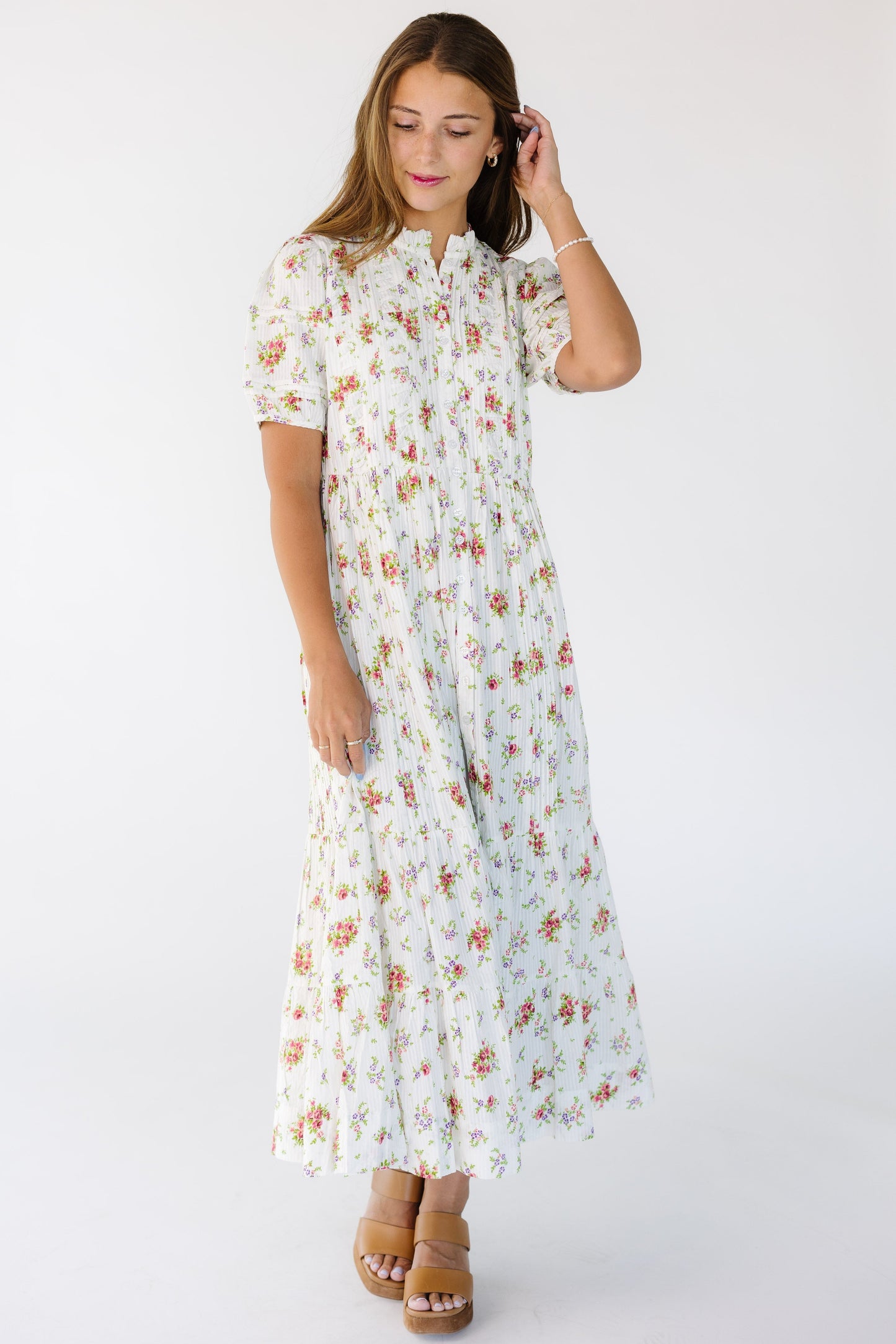 Young woman wearing a white midi-maxi dress in a multicolor floral print with pleats and a tiered skirt.