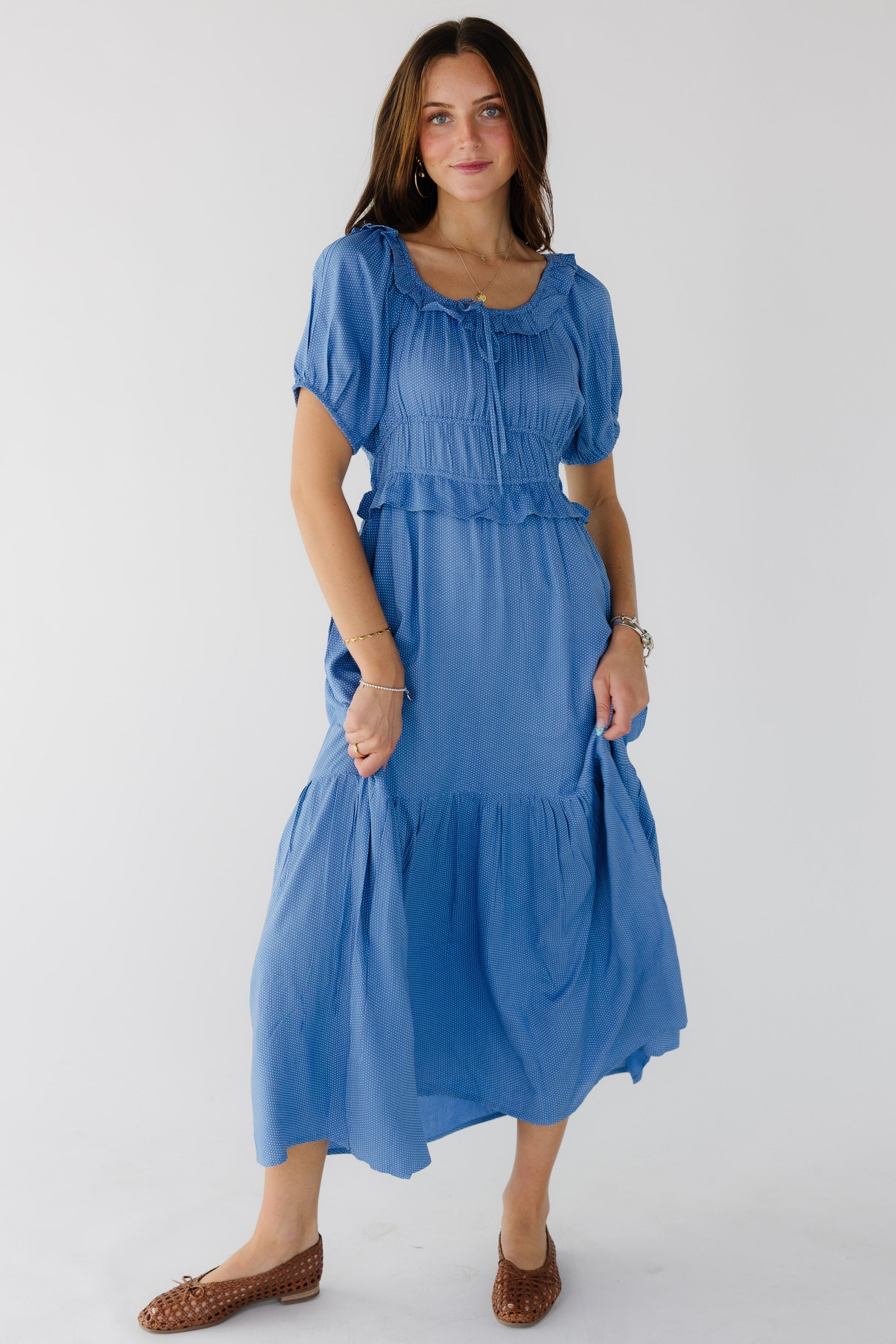 Young woman wearing a modest light blue polka dot dress wtih a ruffled scoop neckline, short puff sleeves, wide waistband with  ruffle and a wide bottom ruffle.