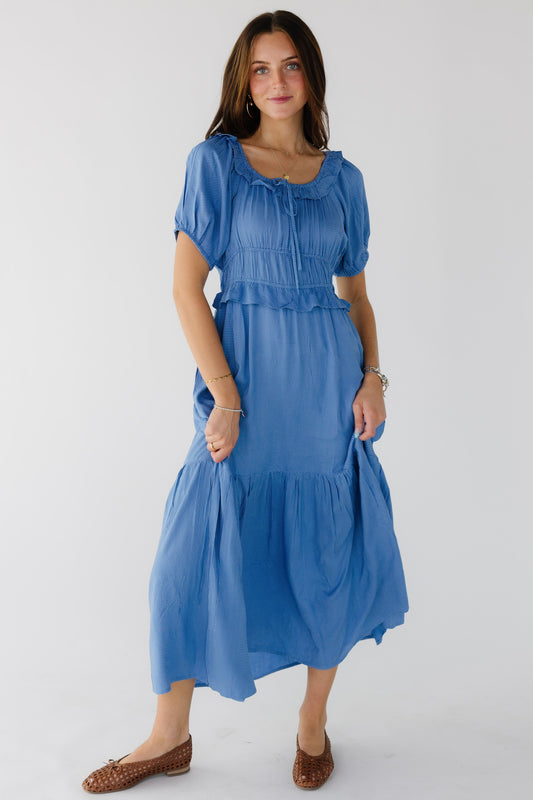 Young woman wearing a modest light blue polka dot dress wtih a ruffled scoop neckline, short puff sleeves, wide waistband with  ruffle and a wide bottom ruffle.