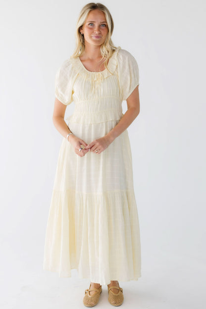 Woman wearing a light yellow midi-maxi dress with a scop neckline and puff sleeves.