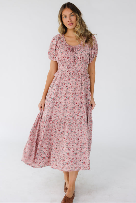Young woman wearing a lovely pink floral midi dress with a scoop neckline, short puff sleeves, wide waistband and a full skirt. 