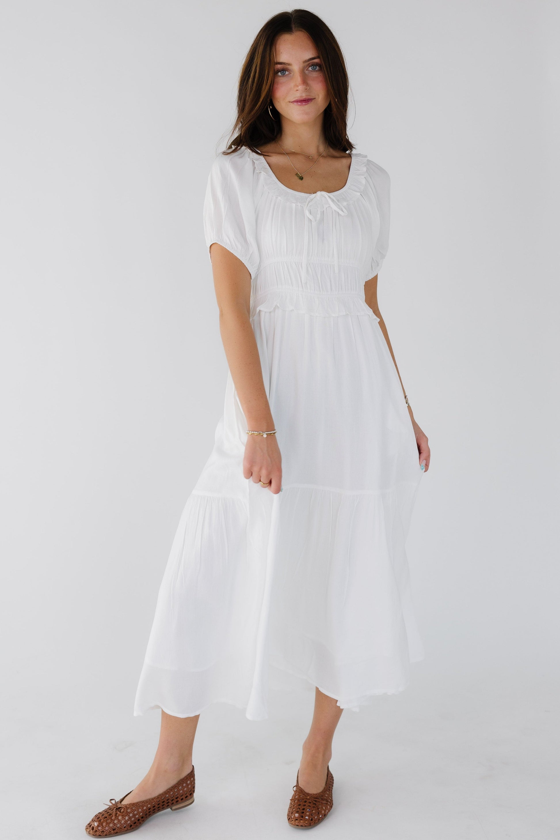 Young woman wearing a modest white midi dress wtih a scoop neckline, short puff sleeves and a wide ruffled neckline.