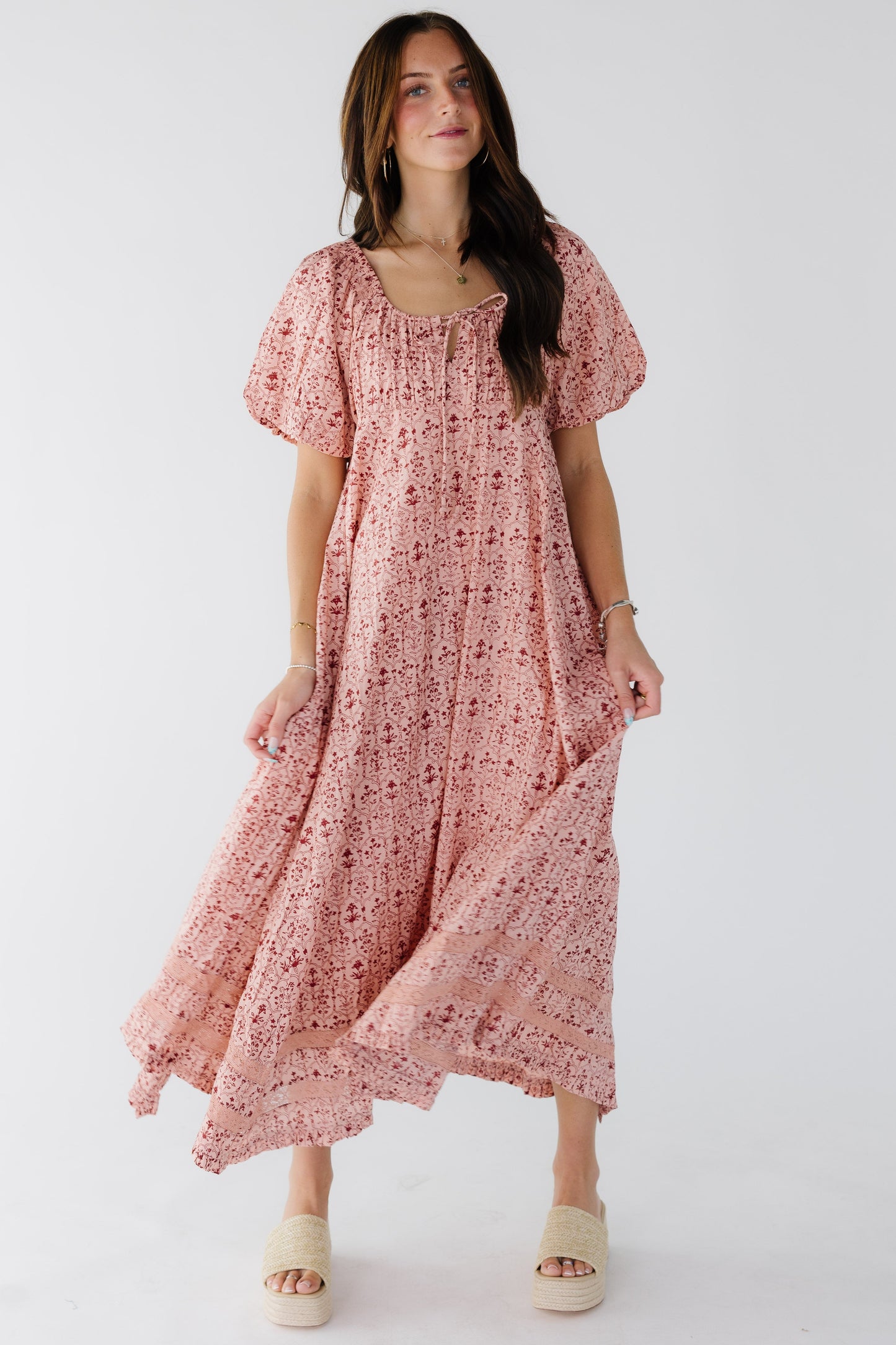 Woman wearing an empire waist dress with a full kercheif hem dress with lace insets, balloon sleeves and a drawstring scoop neckline.