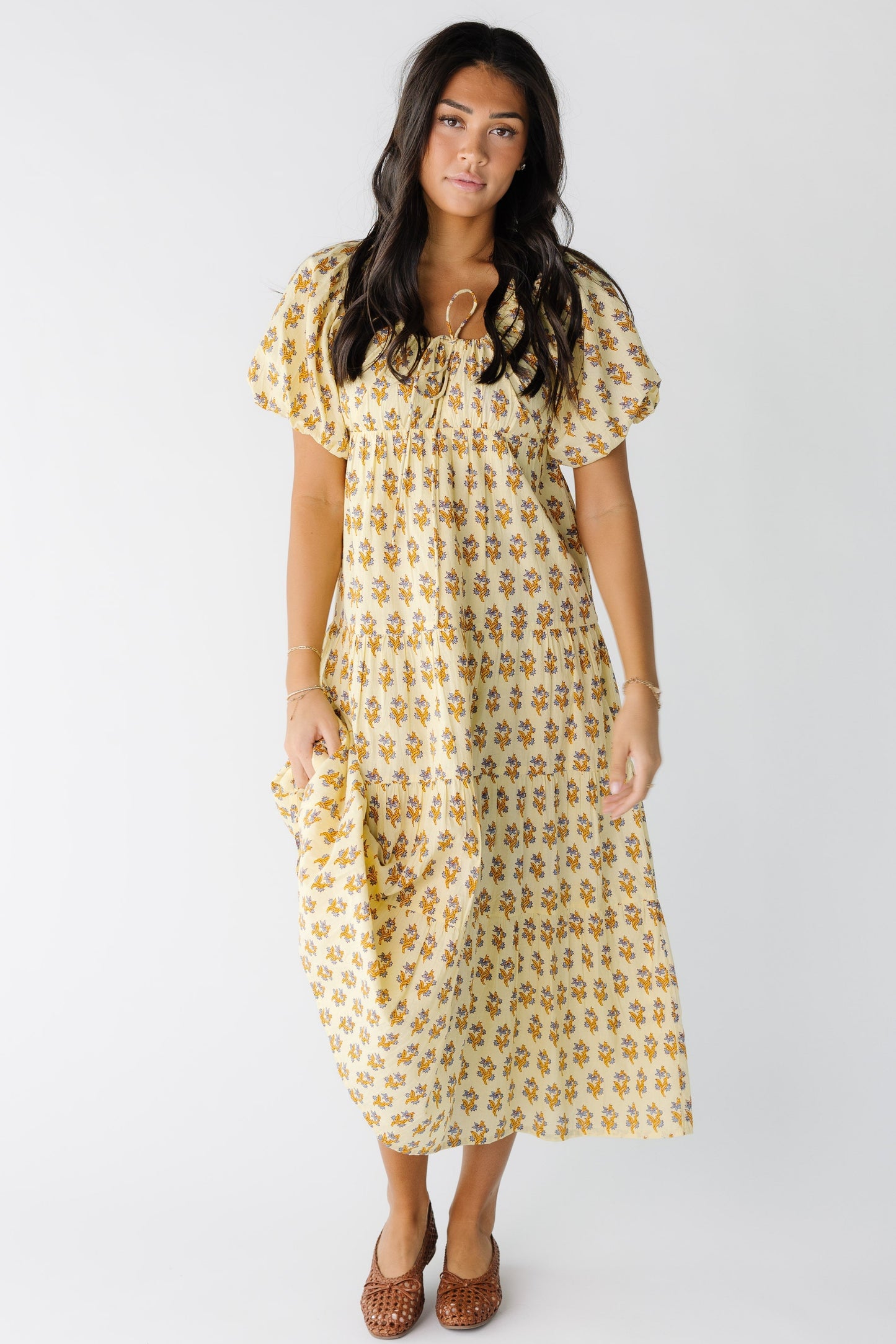 Young woman wearing a yellow floral print midi-maxi dress with a drawstring scoop neckline and large balloon sleeves.