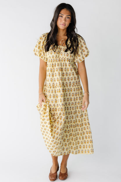 Young woman wearing a yellow floral print midi-maxi dress with a drawstring scoop neckline and large balloon sleeves.