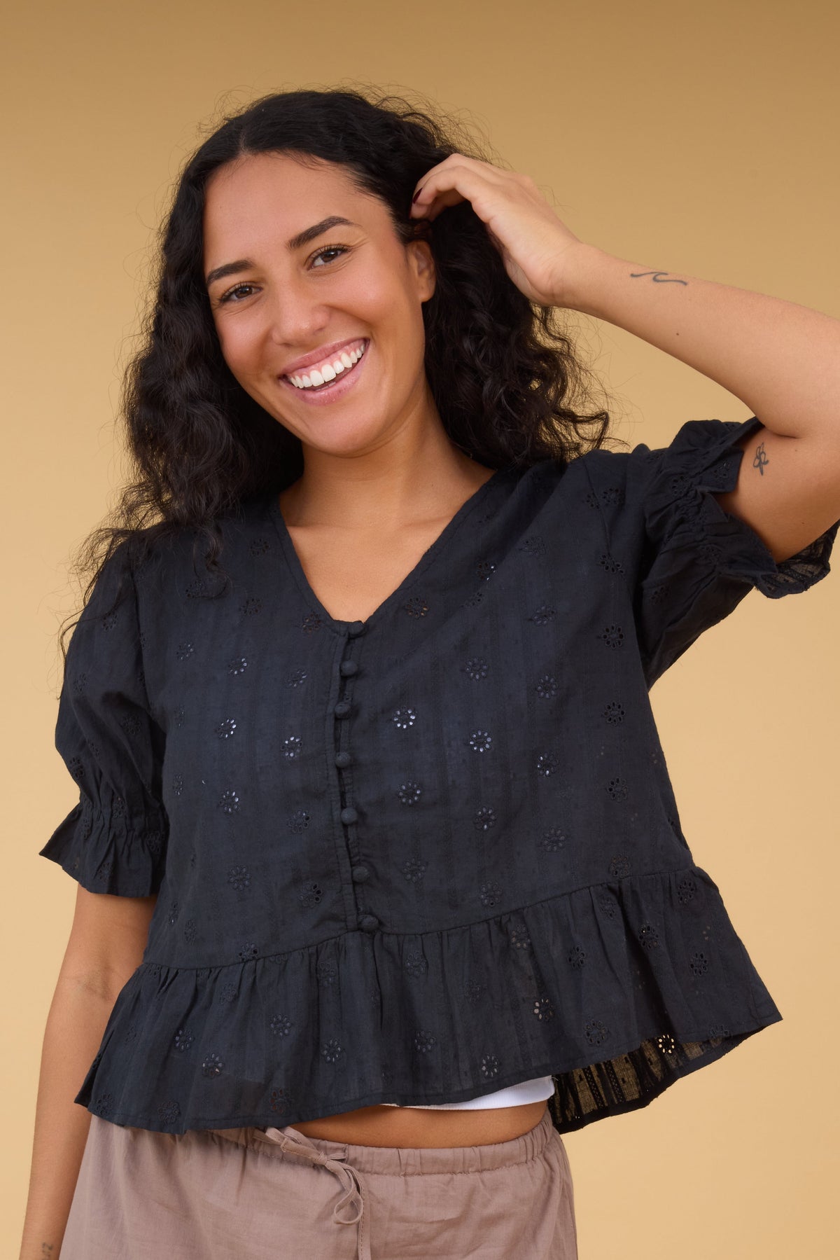 Woman wearing a black eyelet blouse with a V-neckline, short puff sleeves and front buttons.