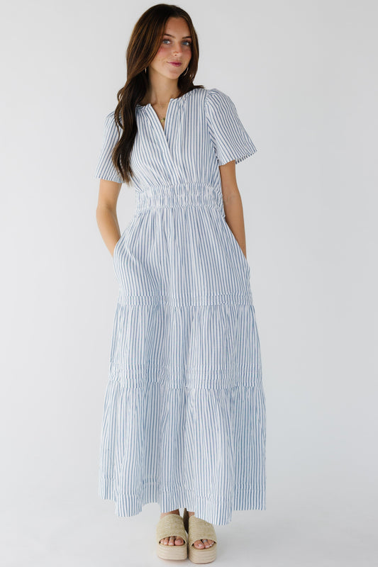 Young woman wearing a modest white and blue stripe tiered midi-maxi dress with a wide elastic waist, shrot sleeves and a V-neckline.
