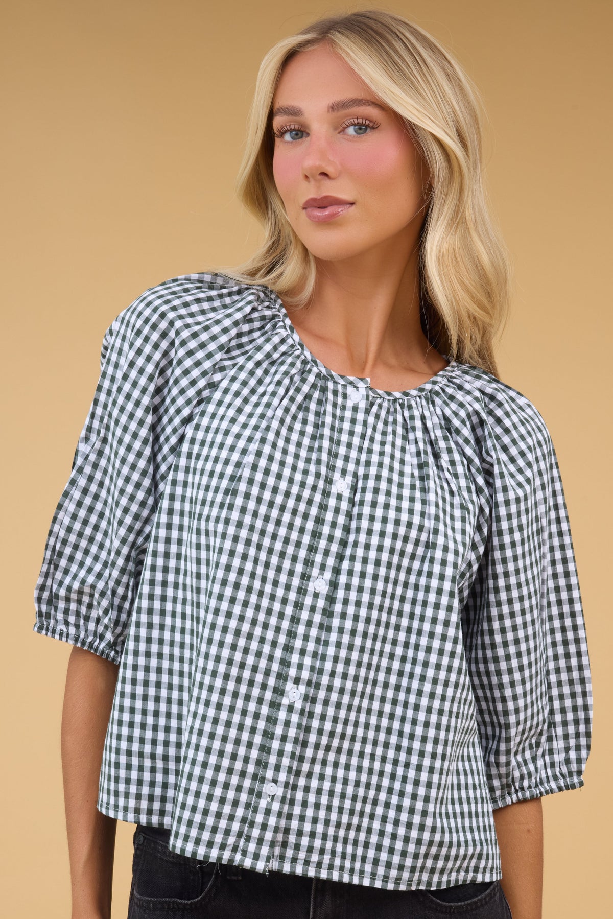 Young woan wearing a modest green gingham, button down blouse with half length sleeves.
